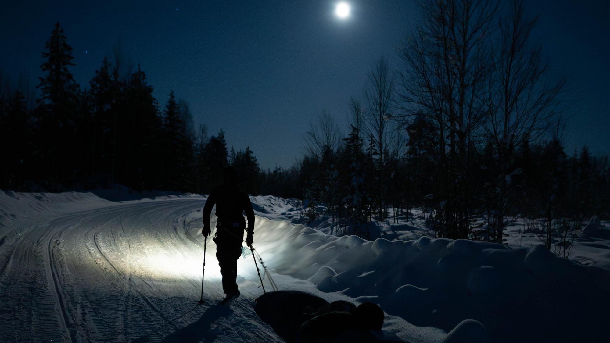 Rob Wilkinson hauling a pulk along a moonlit snow track
